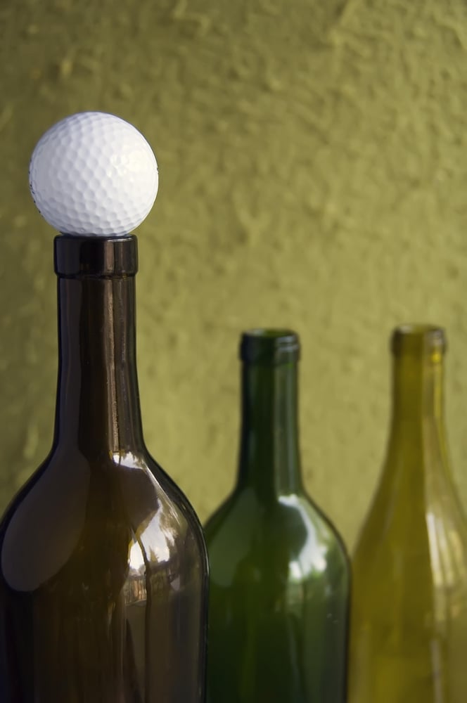 Golf ball on mouth of empty wine bottle (focus on golf ball)